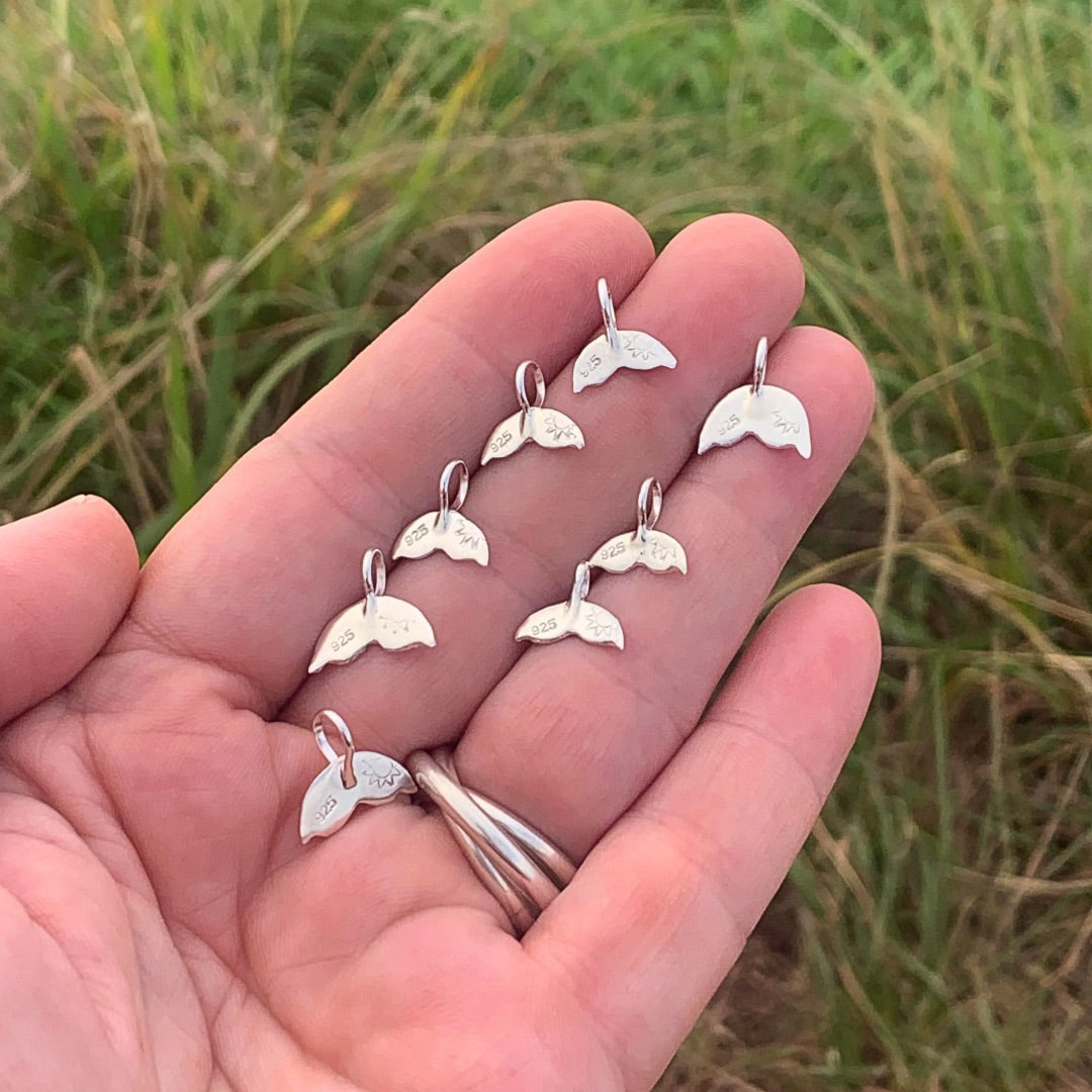 Ray of Sunshine Jewellery - hand made whale tails on my open hand with a green grassy headland in the background.