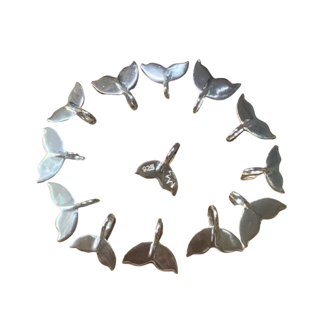 Ray of Sunshine Jewellery - 13 of my hand forged whale tails in a laying side by side in a circle it’s a white background. The centre one has a stamped 925 and dash of sunshine