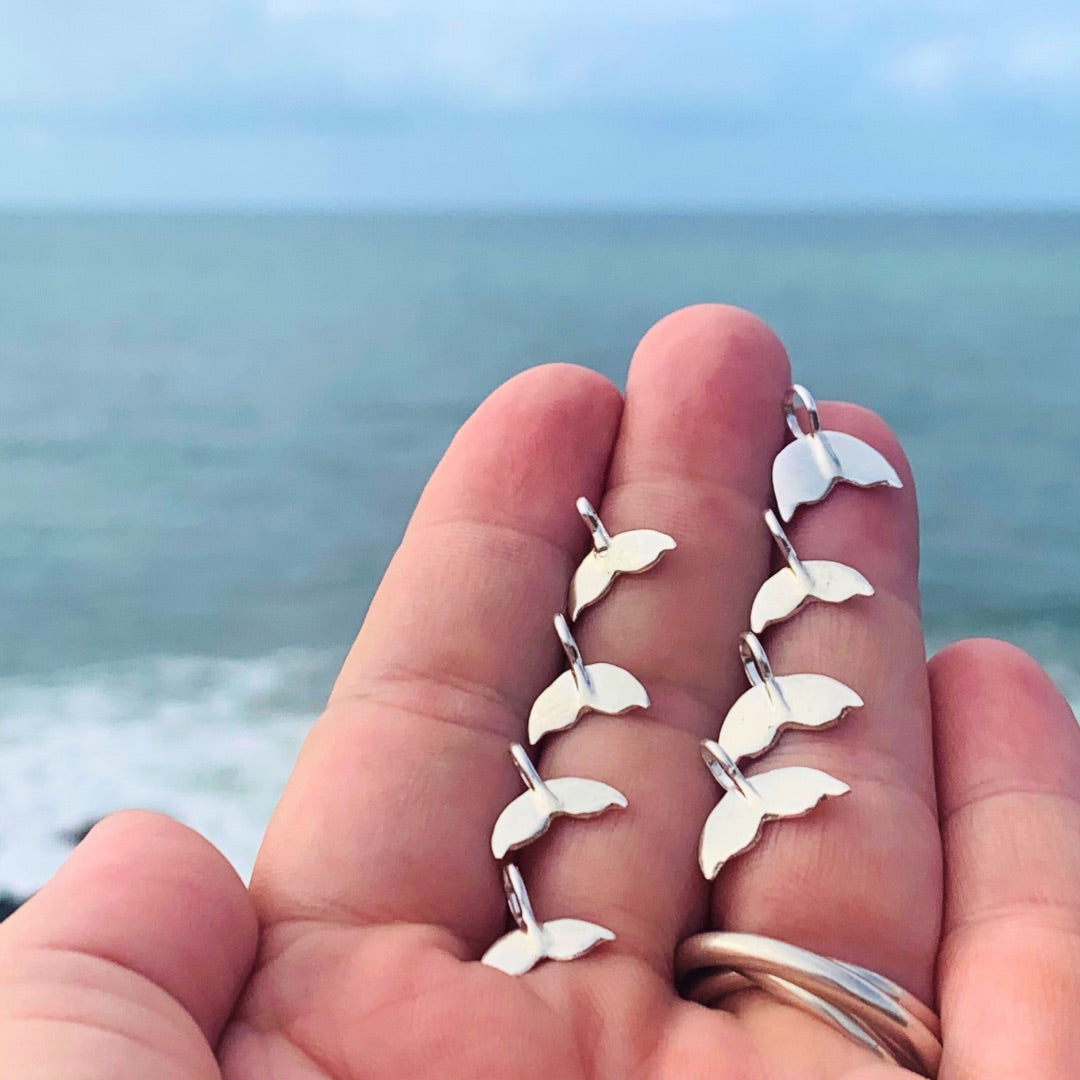 Ray of Sunsine Jewellery - hand forged Silver whale tails on my open hand over looking the ocean.