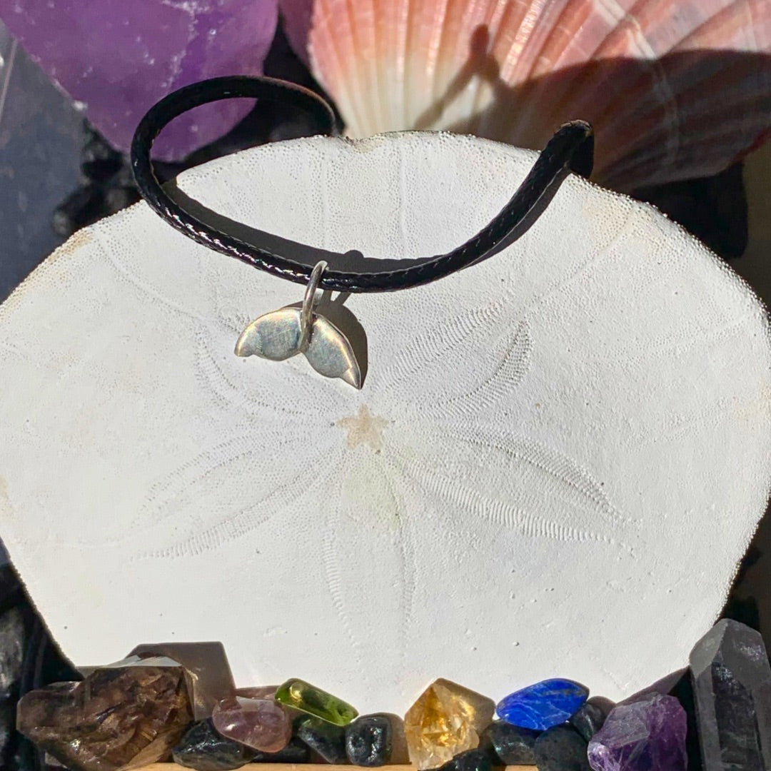 Ray of Sunshine Jewellery - my hand made Sterling Silver whale tail hanging from a black cord nestled on a sand dollar shell surrounded by pink shells and colourful gemstones