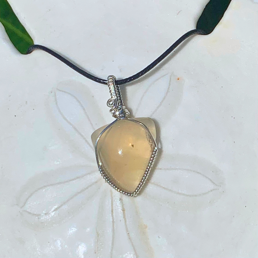 Ray of Sunshine Jewellery natural golden citrine tri shaped stone is hugged in sterling silver and hangs on a giant sand dollar shell in the sunshine