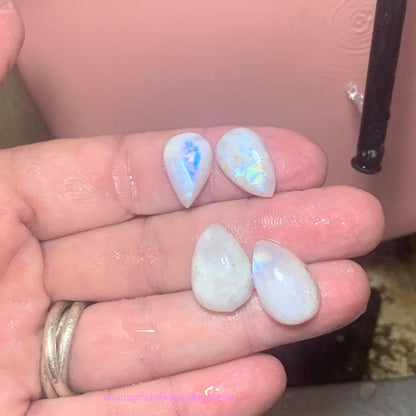 Four light blue moonstone stones held in a hand against a pink polishing pad background