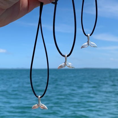 RAY OF SUNSHINE JEWELLERY - 3 HAND MADE NECKLACES ARE HANGING FROM BLACK CORDS IN THE SUNSHINE OVER THE OCEAN BLUE WATER