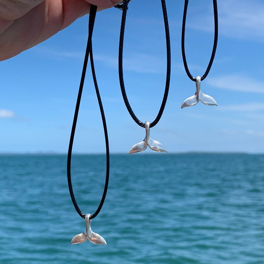RAY OF SUNSHINE JEWELLERY - 3 HAND MADE NECKLACES ARE HANGING FROM BLACK CORDS IN THE SUNSHINE OVER THE OCEAN BLUE WATER