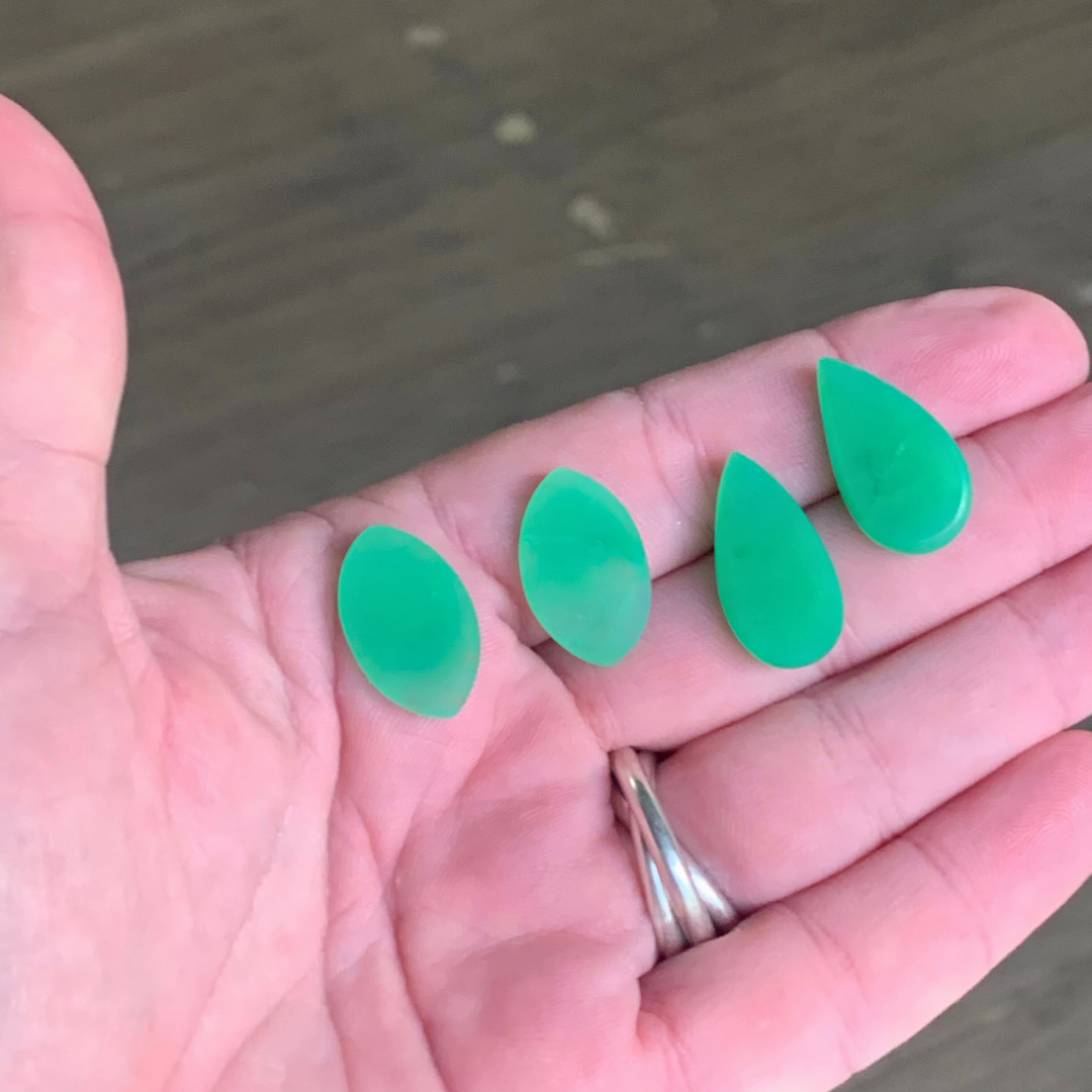 Ray of Sunshine Jewellery- fresh off the polishers, four apple-green teardrop-shaped gemstones held in a hand with a blurred background