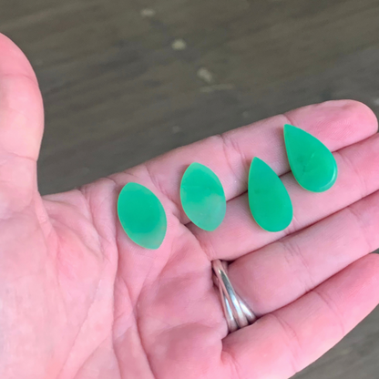 Ray of Sunshine Jewellery- fresh off the polishers, four apple-green teardrop-shaped gemstones held in a hand with a blurred background