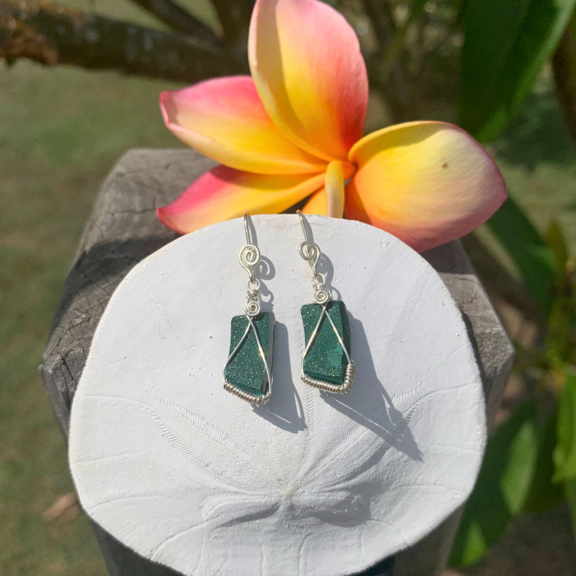 Ray of Sunshine Jewellery- green Druzy Malachite earrings on a white sand dollar shell with a colorful flower in the background