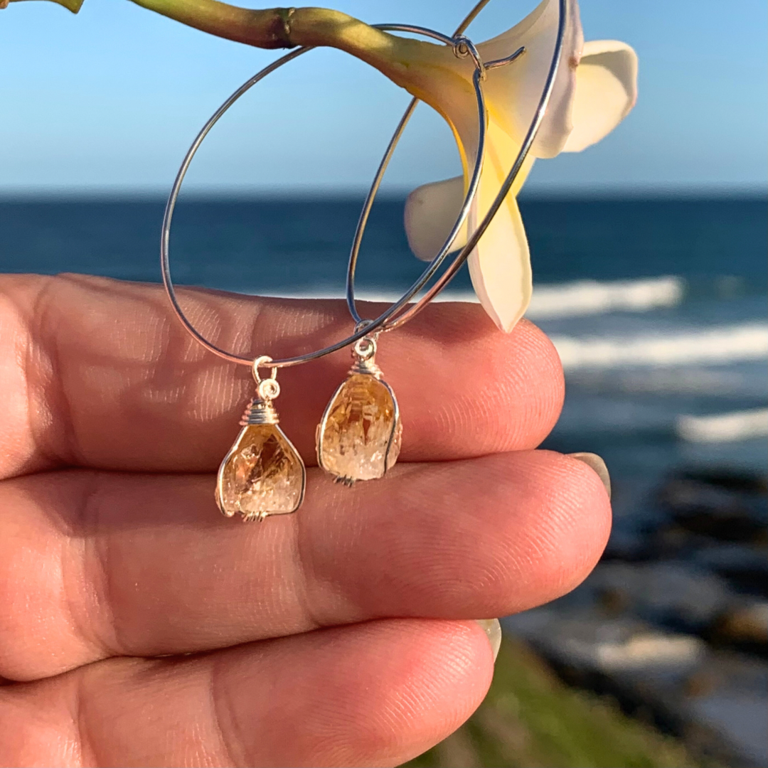 Ray of Sunshine Jewellery- Hoop earrings with teardrop-shaped Citrine crystal points  held against a beach background