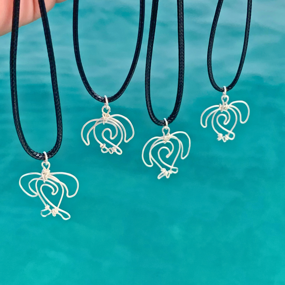 Four necklaces with handmade sea turtle against a teal ocean water background, hanging from a black cord. handmade in northern nsw, Australia.
