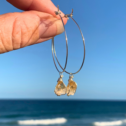 Ray of Sunshine Jewellery- Sterling Silver hoop earrings with teardrop-shaped golden Citrine crystal points held against a blue sky and ocean background. 