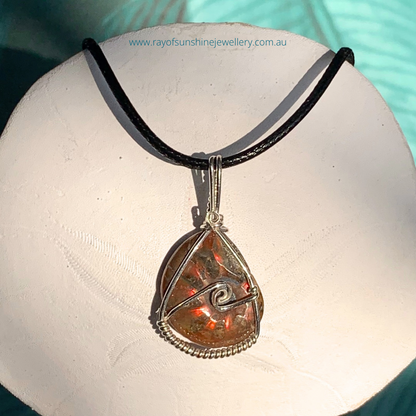 Ray of Sunshine Jewellery- Ammonite pendant with red flash of colour on a white sand dollar shell with a blurred background