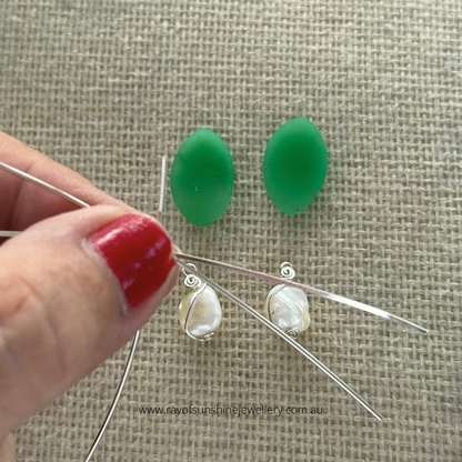 Ray of Sunshine Jewellery-!Apple-Green Chrysoprase earrings being held by a hand with red nail polish on a textured beige background.  Wire wrapping in the making.