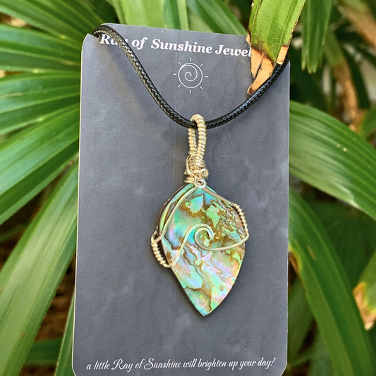 Multicolored nz paua shell pendant wrapped in silver wire on a gray card with green leaves in the background