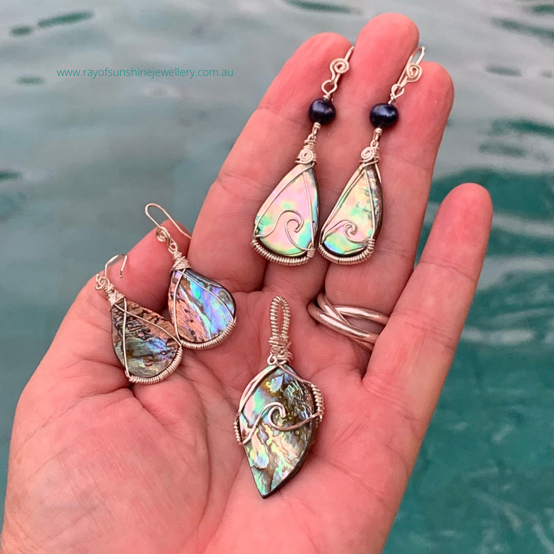 Hand holding multicoloured albalone shell jewelry set with watery background.