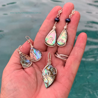 Hand holding multicoloured albalone shell jewelry set with watery background.