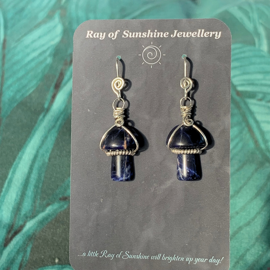 Ray of Sunshine Jewellery- Pair of blue Sodalite mushroom-shaped earrings on a 'Ray of Sunshine Jewellery' business card with green leaves in the background.