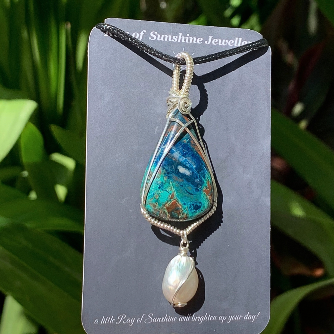 Turquoise blue Azurite Chrysocolla and pearl pendant with silver wire wrapping on a ‘Ray of Sunshine Jewellery’ card against a green leafy background.