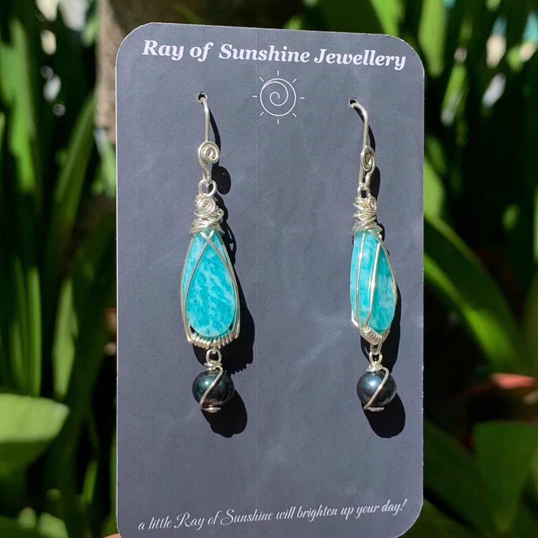 Turquoise blue amazonite and tahitian black pearl earrings on a 'Ray of Sunshine Jewellery' card with green foliage in the background