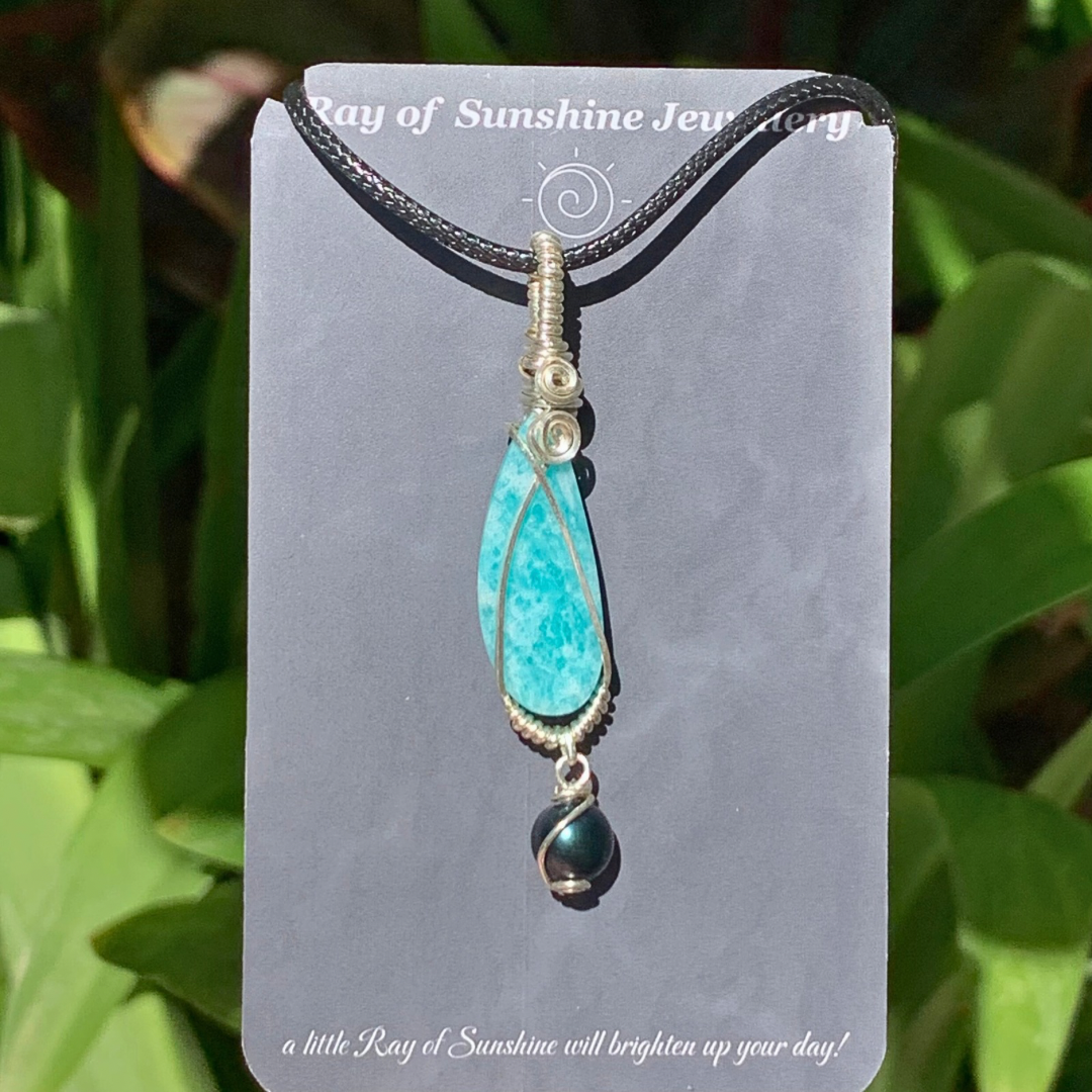 Turquoise amazonite pendant with a black tahitian pearl wrapped in silver wire on a gray ‘Ray of Sunshine Jewellery’ card with green leaves in the background
