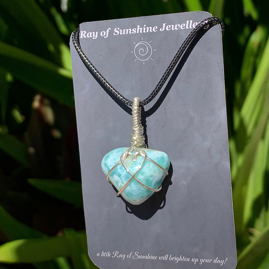 Swirly blue green gemstone necklace with a silver wire heart on a ‘Ray of Sunshine Jewellery’ card with green foliage in the background