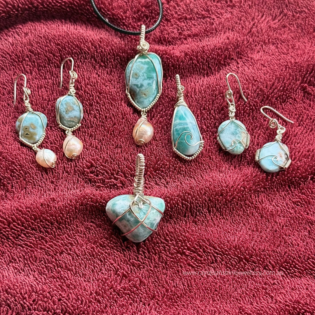Multiple larimar jewellery pendants wrapped in silver wire and earrings on a red fabric background