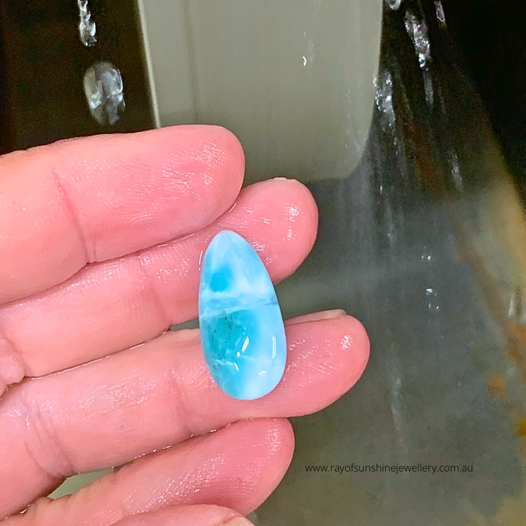 Dreamy blue oval larimar gemstone held between fingers under a wet grinding wheel whilst being shaped by me