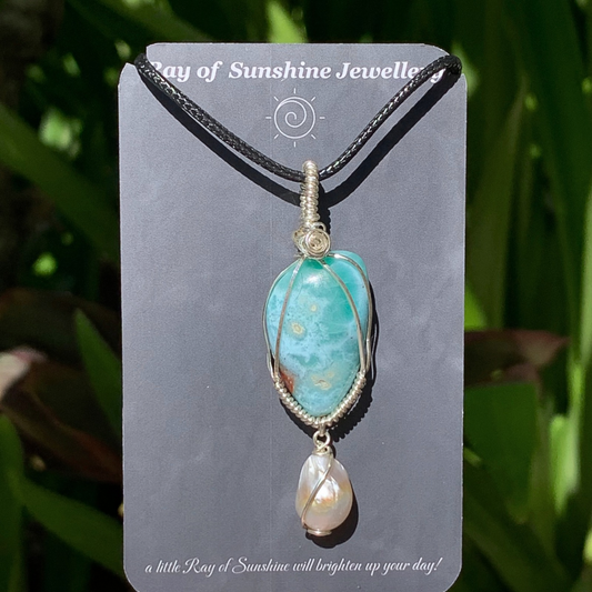 Blue green larimar pendant and baroque white pearl necklace on a ‘Ray of Sunshine Jewellery’ card with greenery in the background
