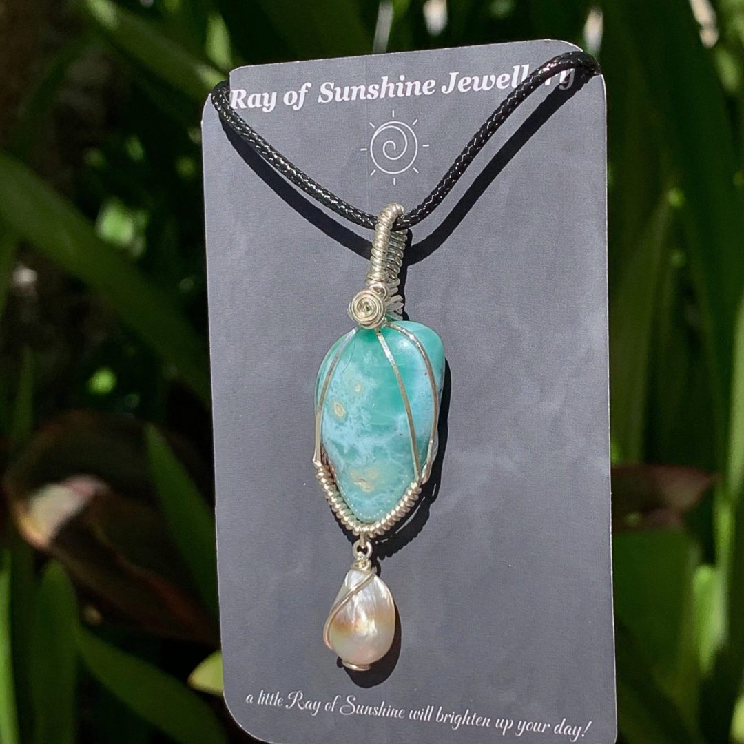 Blue green larimar pendant with pearl on ‘Ray of Sunshine Jewellery' branding card, against a green leafy background.