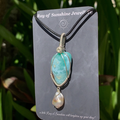 Blue green larimar pendant with pearl on ‘Ray of Sunshine Jewellery' branding card, against a green leafy background.