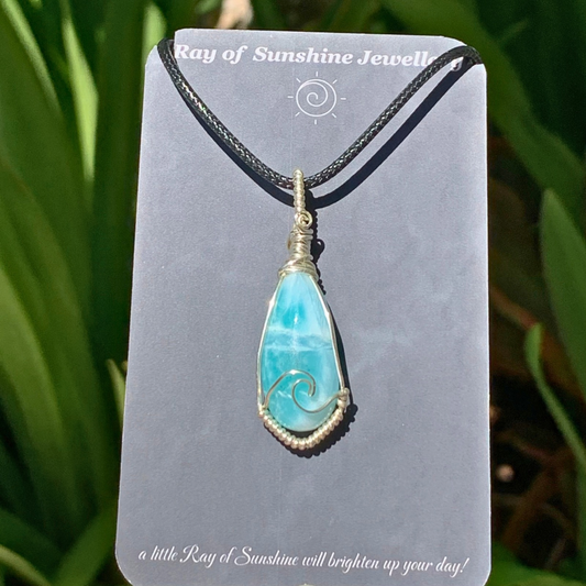 Blue green larimar gemstone necklace on a  'Ray of Sunshine Jewellery’ card, against a green leafy background.