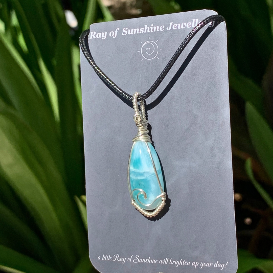 Blue green larimar wrapped pendant on a 'Ray of Sunshine Jewellery’ card against a green leafy background