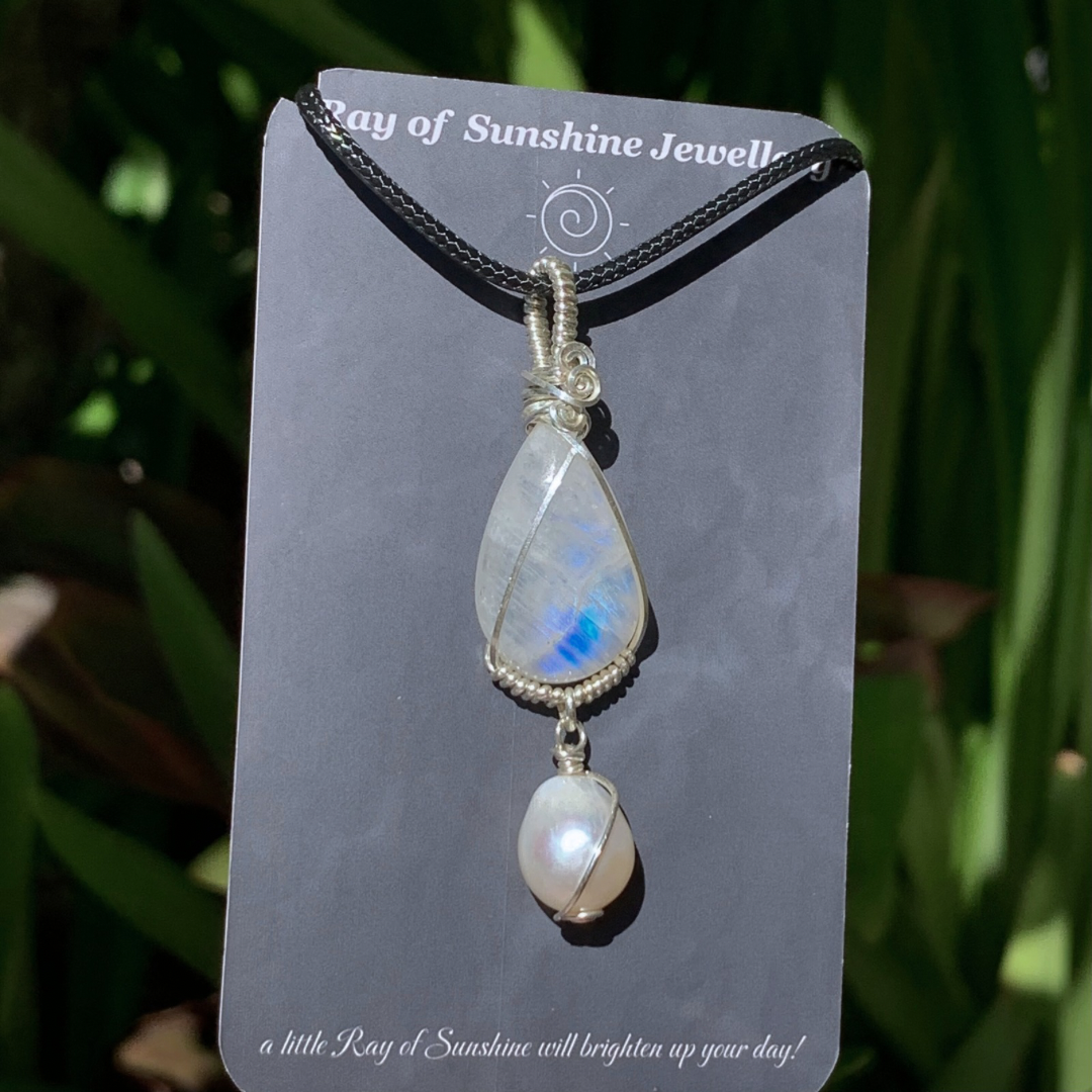 Flashy blue moonstone and pearl pendant on a ‘Ray of Sunshine Jewellery’ card with green foliage in the background