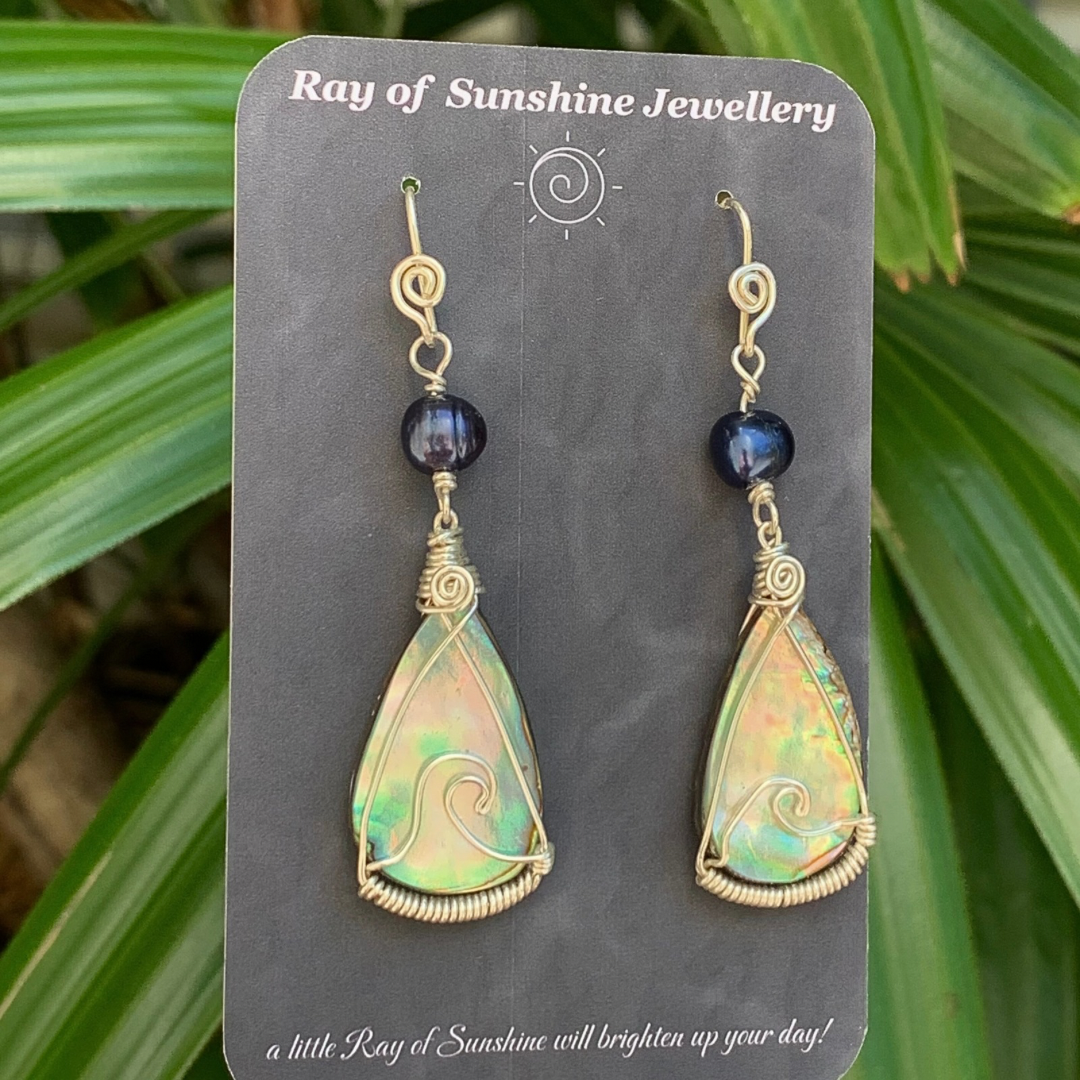 Pair of multicoloured teardrop earrings with a silver wave shape wire across each shell on a 'Ray of Sunshine Jewellery' card with green leafy background