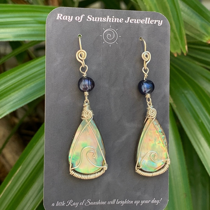 Pair of multicoloured teardrop earrings with a silver wave shape wire across each shell on a 'Ray of Sunshine Jewellery' card with green leafy background