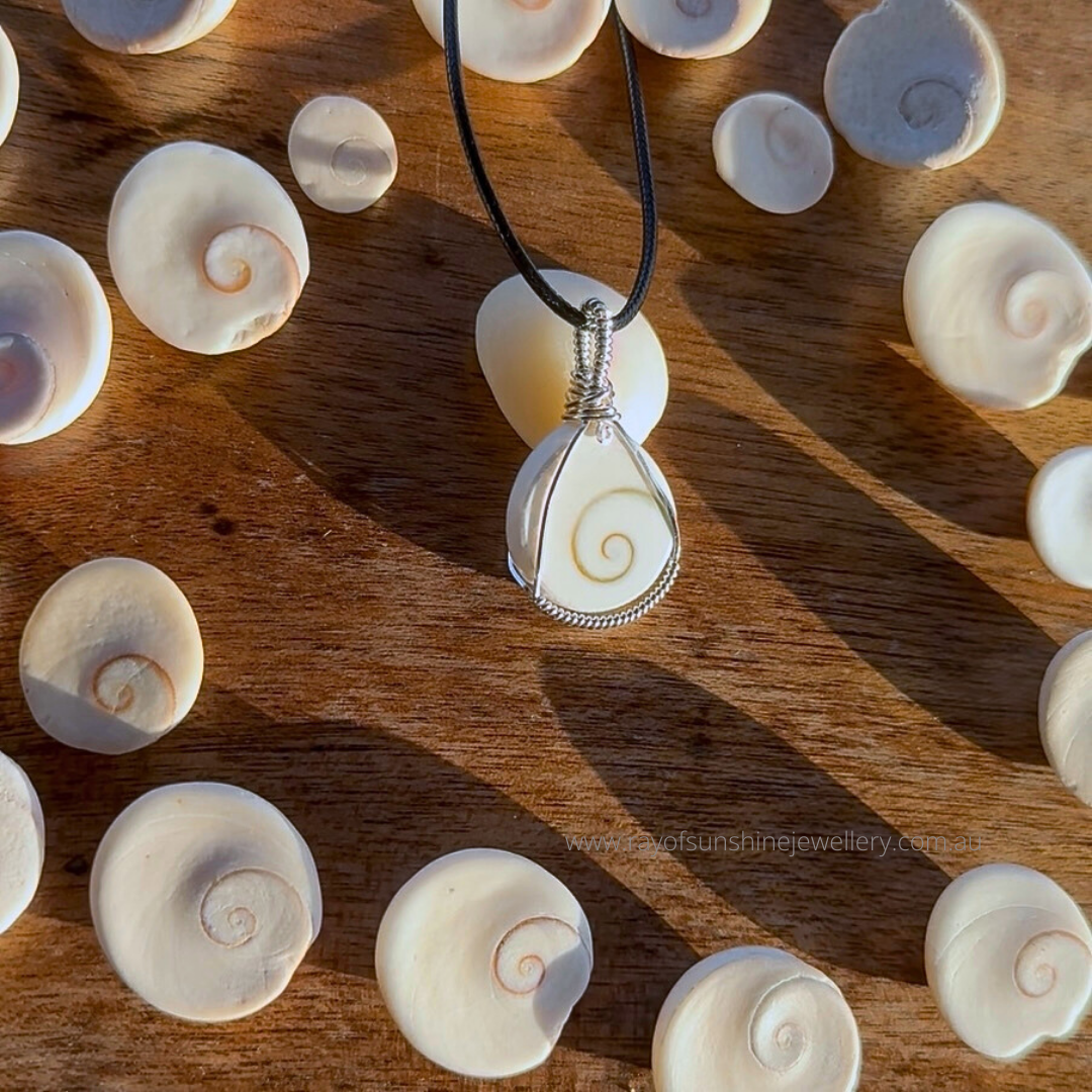 Shell pendant necklace on a wooden surface with raw shells in the afternoon sun shadow