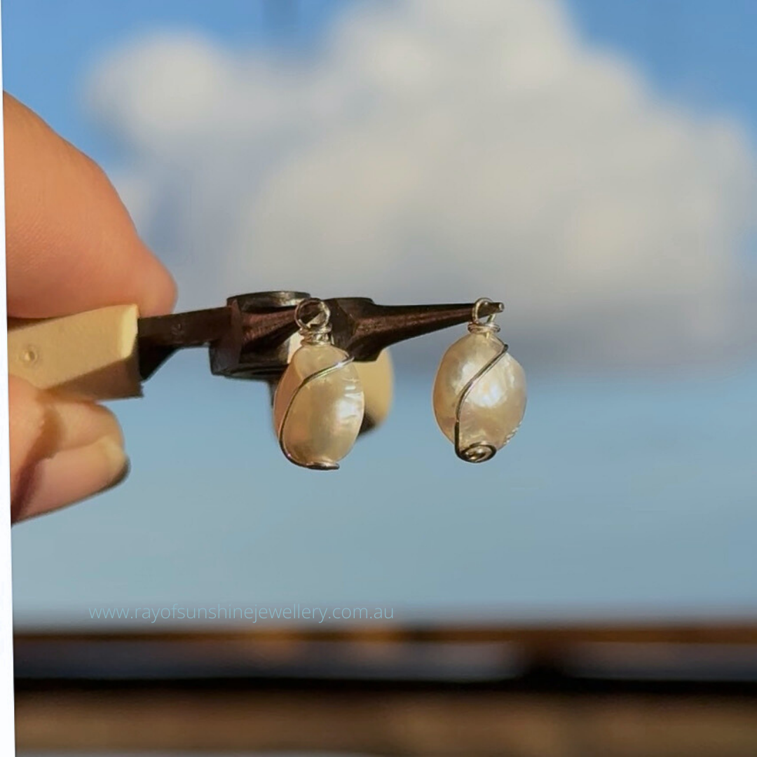 White pearls wrapled in silver wire being worked on with pliers against a blurred outdoor background