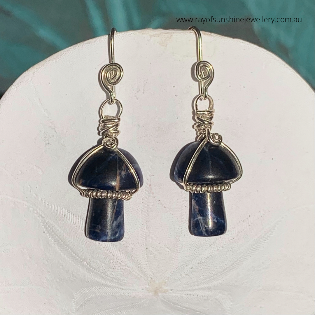 Ray of Sunshine Jewellery- Pair of mushroom-shaped earrings with Sodalite blue gemstones on a white sand dollar shell surface.