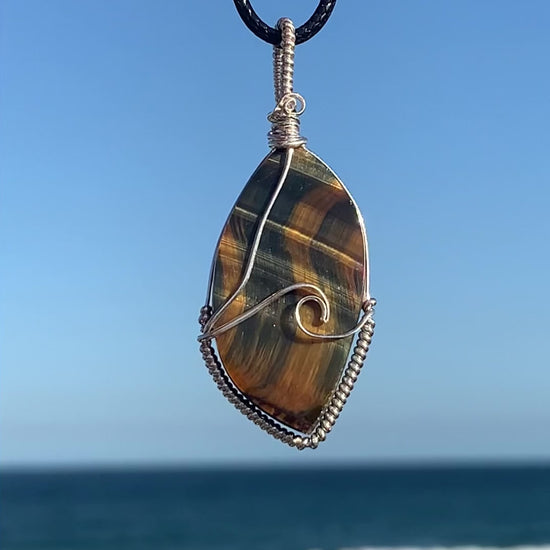 Ray of Sunshine Jewellery this gorgeous surfboard shaped stone has natural blue and gold shimmer that dances across the stone in a wave like pattern. Paired with my sterling silver wave of the day, this necklace is a statement piece. Pictured overlooking the ocean in the sunshine. Video captures the shimmer of gold and blue dance across the stone as it twists from one side to the other