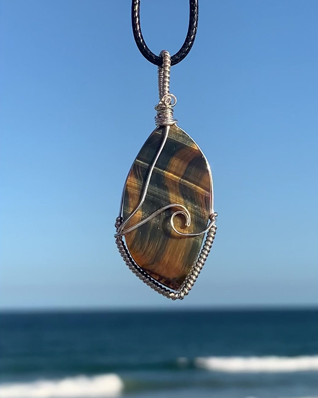 Ray of Sunshine Jewellery this gorgeous surfboard shaped stone has natural blue and gold shimmer that dances across the stone in a wave like pattern. Paired with my sterling silver wave of the day, this necklace is a statement piece. Pictured overlooking the ocean in the sunshine. Video captures the shimmer of gold and blue dance across the stone as it twists from one side to the other