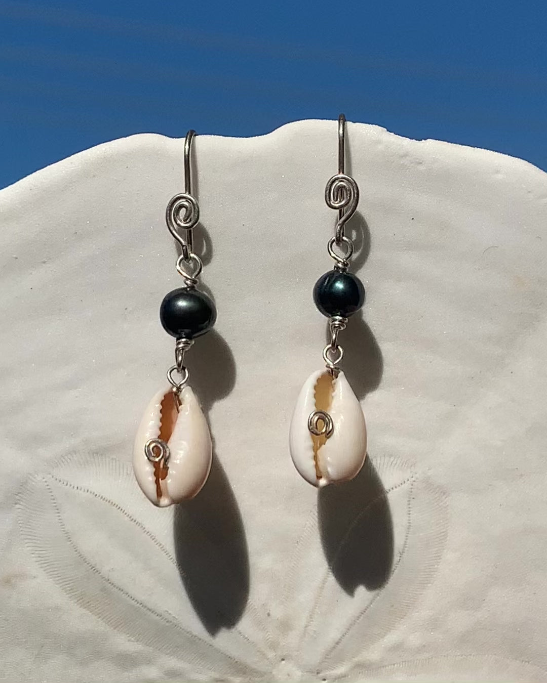 Ray of Sunshine Jewellery- earrings are dancing in the sunlight and hanging from a white sand dollar shell with lovely blue sky in the background