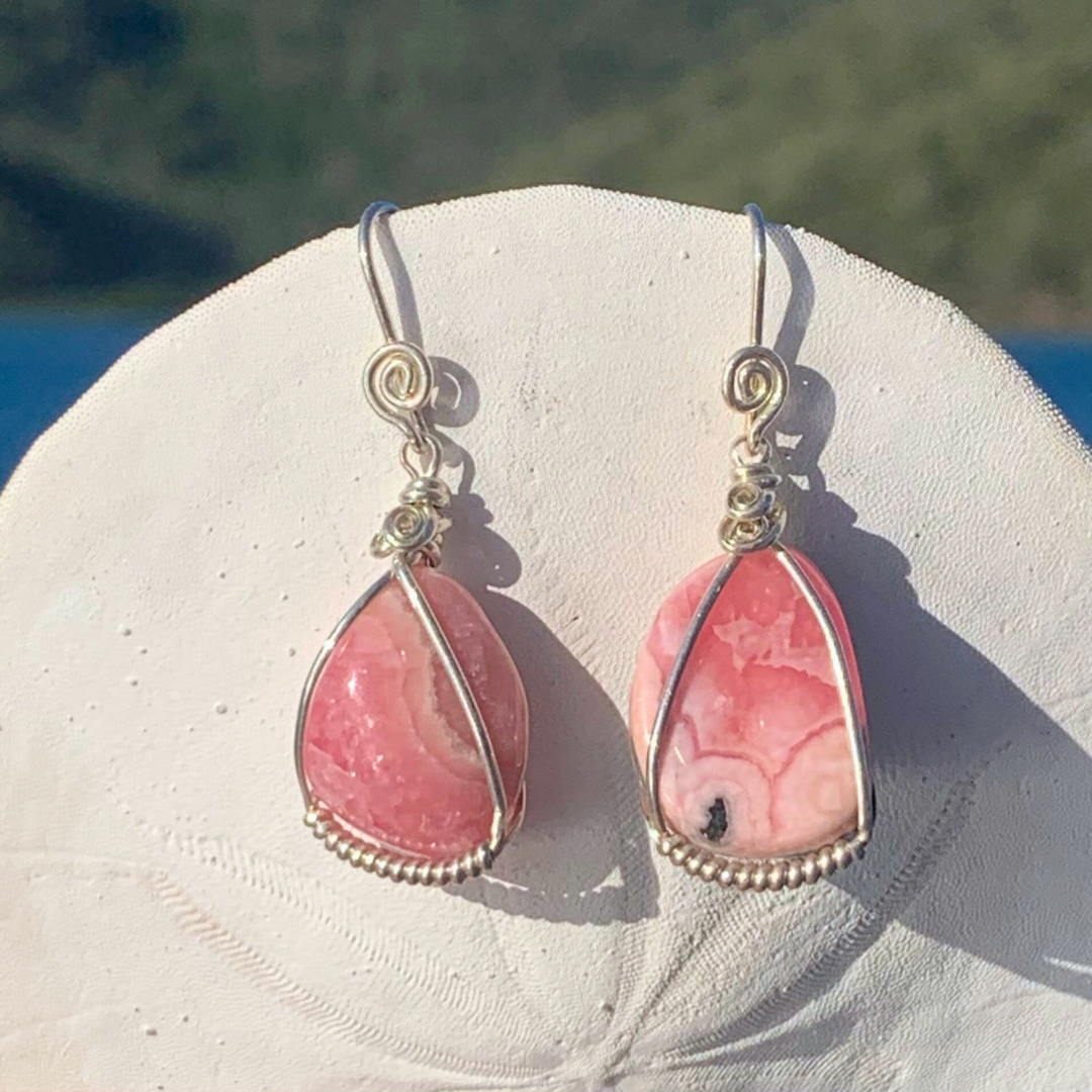 Ray of Sunshine Jewellery - a lovely pair of pink Rhodochrosite Sterling Silver wrapped gemstone earrings hanging from a sand dollar shell in the sun